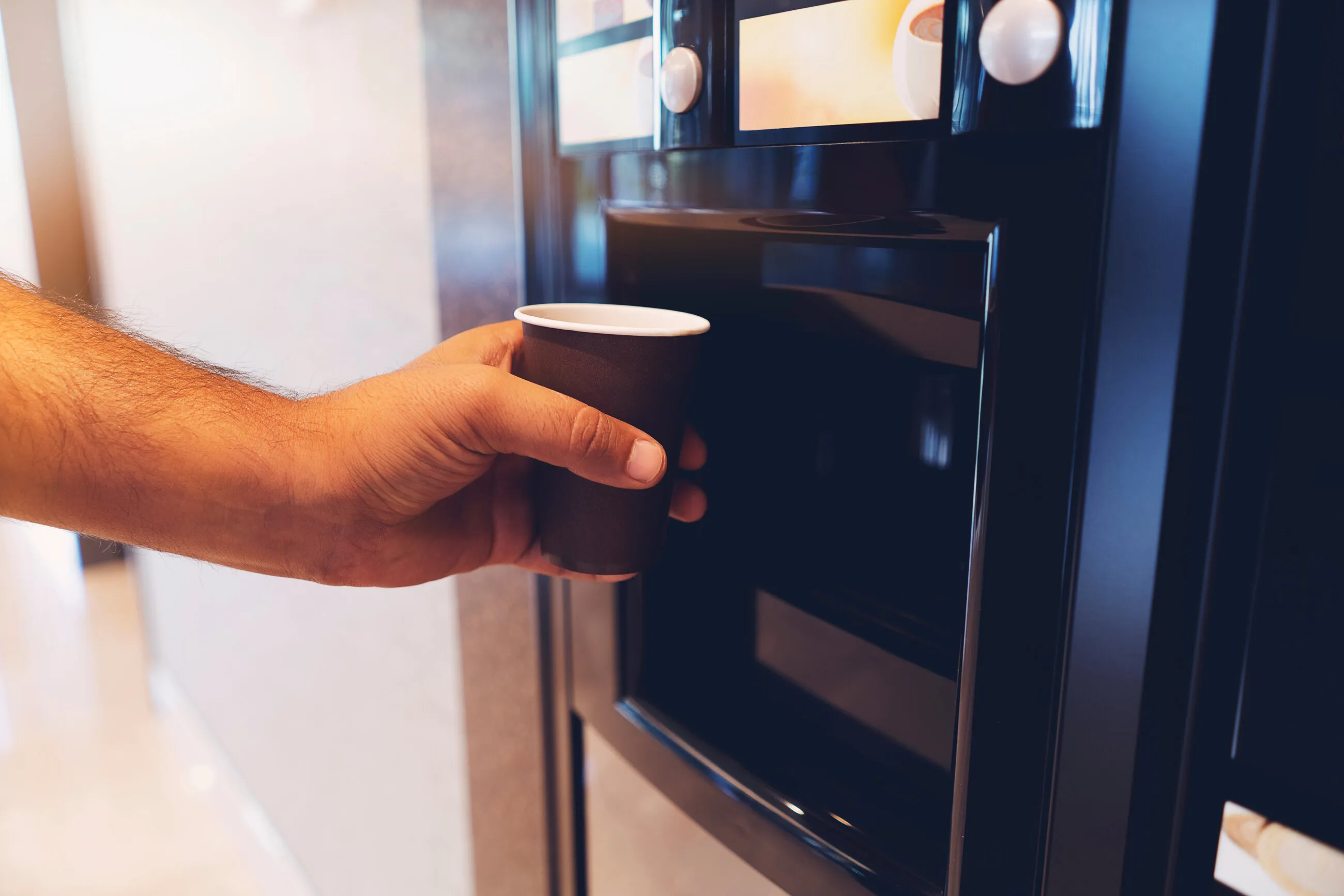 Hand nimmt einen Kaffeebecher aus einem Kaffeeautomaten