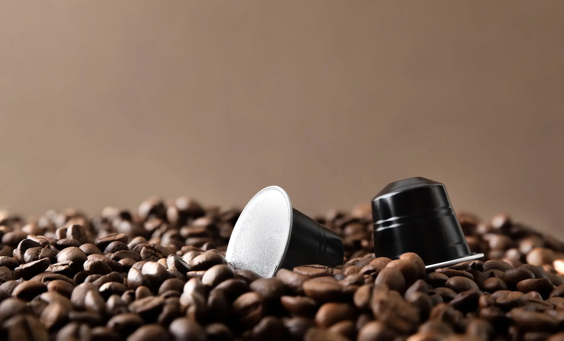 Zwei Kaffeekapseln liegen auf gerösteten Kaffeebohnen