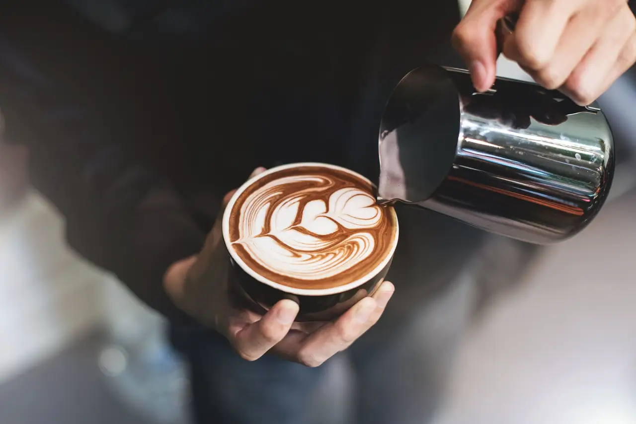 Barista gießt Milchschaum in eine Tasse Cappuccino mit Latte-Art