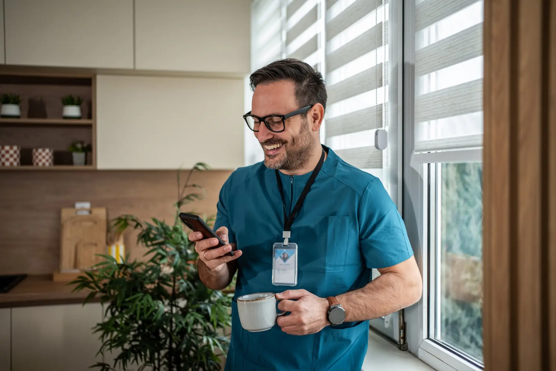 Mitarbeiter mit Kaffeetasse und Smartphone lacht in der Büroküche