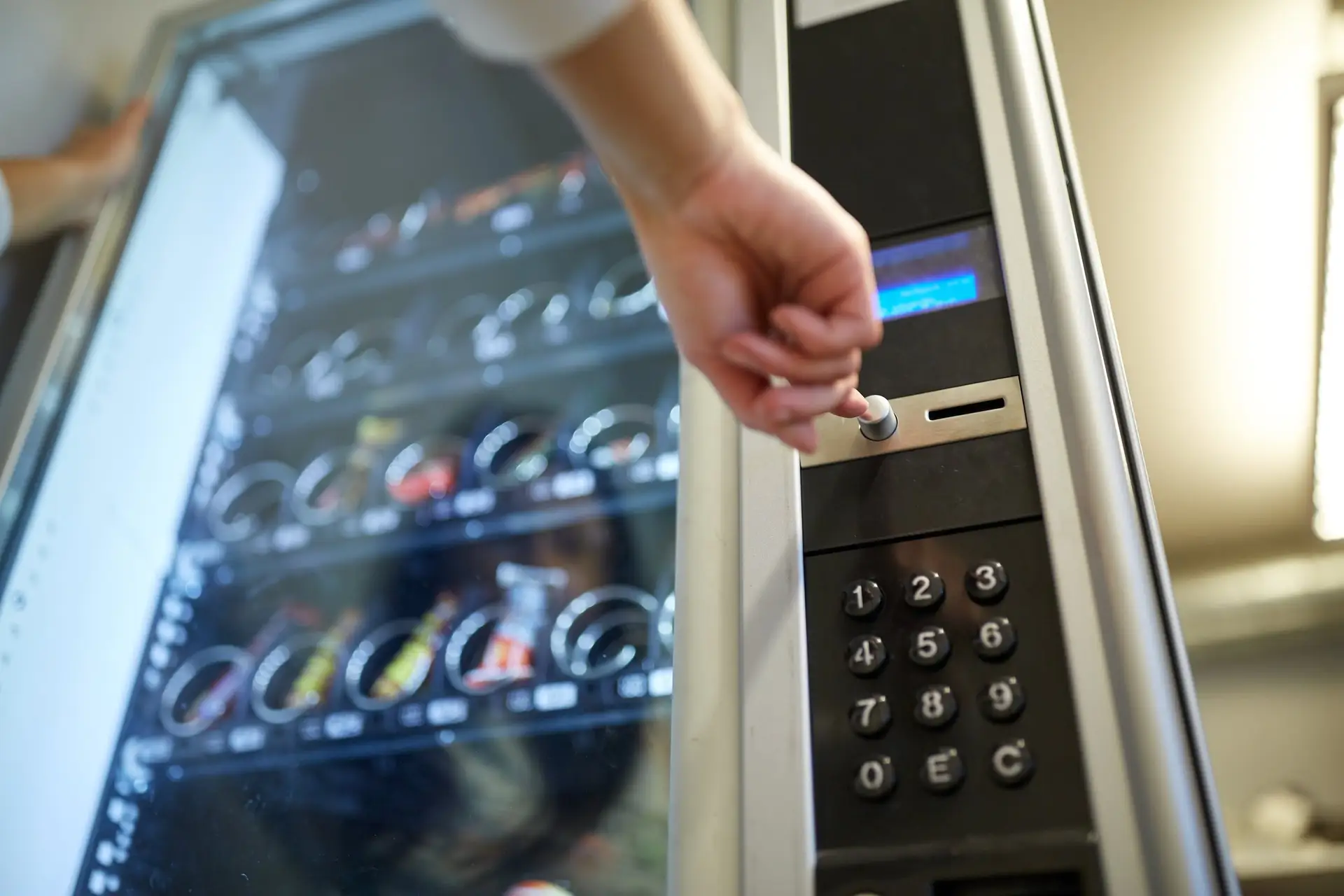 Finger tippt eine Produktnummer in das Tastenfeld eines Snackautomaten