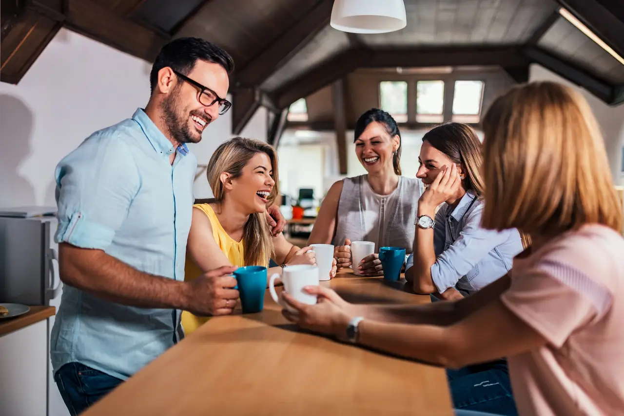 Kolleginnen und Kollegen lachen gemeinsam bei einer Kaffeepause in der Büroküche