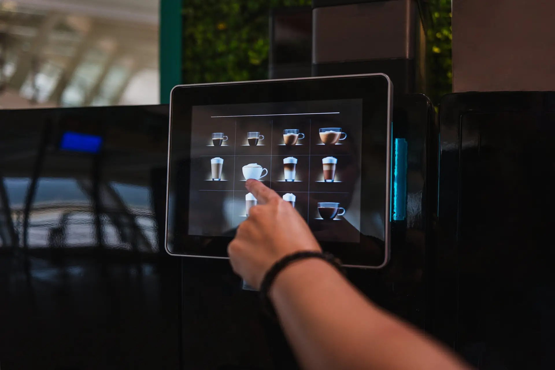 Finger wählt am Touchdisplay eines Kaffeeautomaten ein Getränk aus